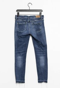 Jean skinny bleu foncé avec une texture délavée. Dispose de cinq poches, d'une étiquette en cuir sur la taille et de détails de bord effiloché.
