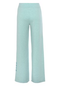 Licht mintgroene wijde broek gemaakt van zachte stof, met een elastische tailleband en het woord "SAND" in een donkerdere blauwe kleur afgedrukt op het linkerbeen.