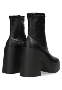 Botas de tobillo de imitación de cuero negro con cierre de cremallera, un tacón alto y afilado, y un acabado suave. El diseño presenta una parte superior sin costuras.