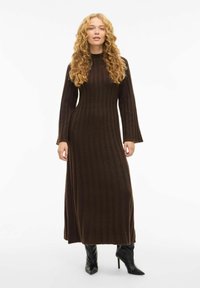 Robe en tricot marron côtelée à manches longues avec un corsage ajusté et des manches évasées, associée à des bottes à talons hauts noires à bouts pointus.