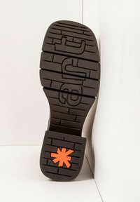 Suela de zapato de goma negra con surcos profundos, que presenta un distintivo acento en forma de estrella naranja en el talón y un patrón de grabado visible.