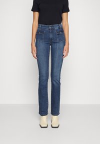 Jeans ajustados de color azul en un lavado medio, con bolsillos frontales y traseros, un corte recto, con un ligero estiramiento y dobladillo a nivel de los tobillos.