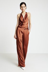 Haut à bretelles en satin marron avec un décolleté drapé, assorti à un pantalon large. Le pantalon est orné d'un bouton décoratif ; le modèle porte des talons blancs.