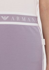 Fioletinė medvilnės mišinė sijonas su baltu elastingu juosmeniu, kuriame užrašyta "ARMANI" pilka spalva. Išskirtinė etiketė šone su "EA" ženklu.