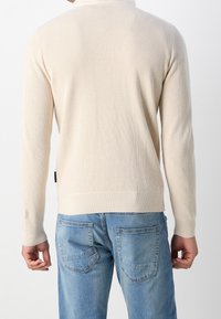 Light beige knit sweater with a textured pattern, featuring long sleeves and a ribbed hem. Worn with light blue jeans.