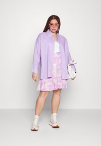 Camisa lilás de botões, top branco, saia franzida rosa tie-dye e sapatilhas brancas com solas castanhas. Acessórios incluem óculos de sol rosa e uma bolsa branca.