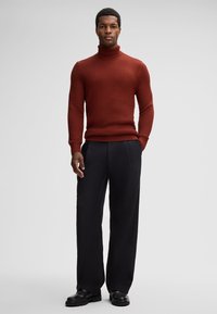 Tkaninowy sweter w kolorze czerwonym z wysokim kołnierzem i dopasowanym krojem, zestawiony z luźnymi czarnymi spodniami i czarnymi butami. Prosty i nowoczesny wygląd.