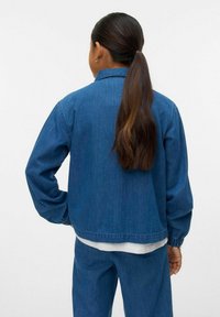 Zila džinsa jaka ar brīvu piegriezumu, kurai ir elastīgas rokas, apkakle un redzamie šuvi. Audumam ir gluda tekstūra un viendabīga krāsa.