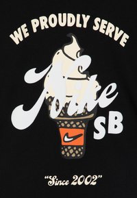 Černé tričko s grafikou zmrzlinového kornoutu se šlehačkou, s nápisem "Nike" bílým písmem a "SB" tučným bílým písmem vedle oranžového loga Nike.