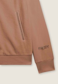 Sweatshirt marrone con una superficie liscia, dotato di una tasca laterale con zip e del nome del marchio "FREDDY" in strass sulla manica.