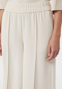Helle, weit geschnittene Hosen aus strukturiertem Stoff. Mit einem elastischen Bund und vertikalen Falten für eine fließende Silhouette.