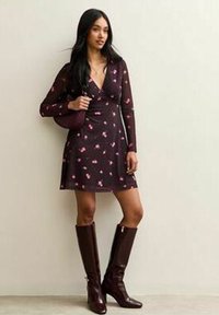 Abito bordeaux scuro con design avvolgente, motivo floreale, maniche lunghe, abbinato a stivali bordeaux al ginocchio e una borsa coordinata.