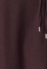 Tessuto bordeaux con finitura testurizzata, caratterizzato da coulisse con accenti metallici. Nessun motivo o grafica presente.