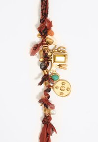 Accesorio con una correa de tela trenzada en color óxido, adornado con charms, cuentas y un colgante circular con detalles florales en tono dorado.