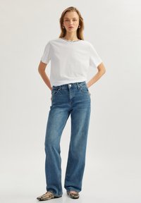 Hvid kortærmet t-shirt med tekstureret krave, parret med lyseblå vide bukser og mønstrede flade sko. Simpelt, afslappet outfit.