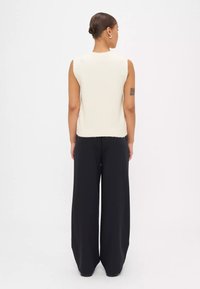 Mouwloze crèmekleurige gebreide top gecombineerd met losse zwarte broeken, met een gladde textuur en een wijd broekontwerp.