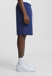 Navy blue cotton shorts with an elastic waistband and white drawstring, paired with white sneakers and crew-length white socks.