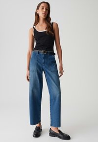 Wijduitlopende blauwe denimjeans met een hoge taille en subtiele stikdetails, gecombineerd met een zwarte tanktop en zwarte instappers.