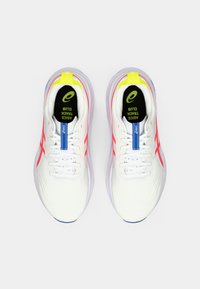 Et par hvite ASICS løpesko med røde striper, gule hælkapper, blå tungeetiketter og svarte innersåler merket "ASICS Track Club."