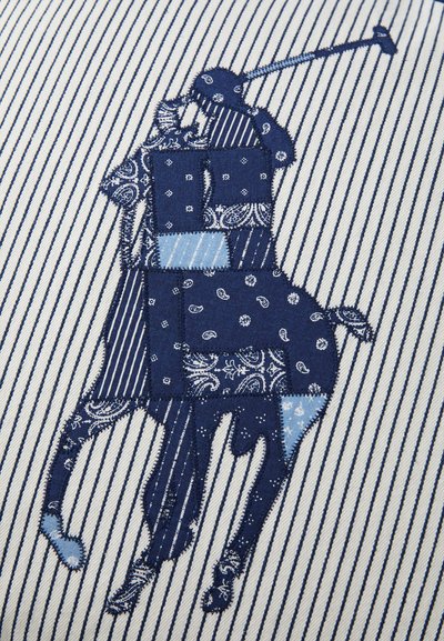 Tamsiai mėlynas ir šviesiai mėlynas siuvinėjimas su polo žaidėju ir arkliu, esantis ant dryžuoto balto fono. Textūruota medžiaga su įmantriomis detalėmis.