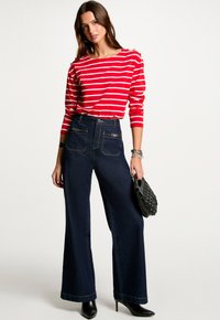 Rot-weißer gestreifter Langarmshirt, hoch taillierte dunkelblaue weite Jeans, mit einer schwarzen Handtasche und Absatzstiefeln.