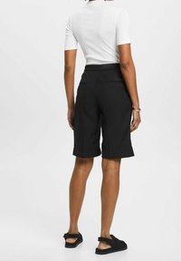 Short Bermuda noir en tissu léger, doté d'une ceinture élastique et d'une coupe décontractée, se terminant juste au-dessus du genou.