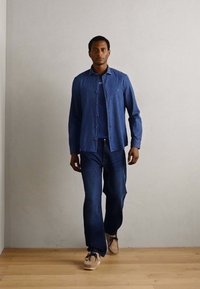 Kék farmering és hozzáillő farmernadrág, alatta egy sima kék pólóval. A ruházat slim fit szabású, világos színű sportcipőkkel párosítva.