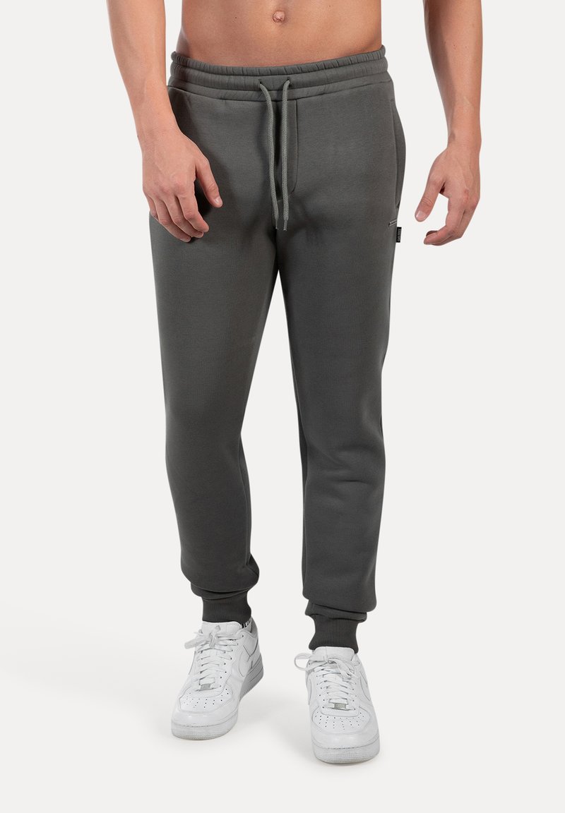 Pantalones de chándal gris oscuro, hechos de una suave mezcla de algodón, con una cinturilla elástica y cordón de ajuste, además de puños de canalé. Combinados con zapatillas blancas.
