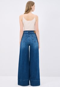 Jeans de tiro alto y pierna ancha en denim azul oscuro, con un ligero desvanecimiento, cinco bolsillos y una etiqueta de cuero marrón en la parte trasera de la cinturilla.