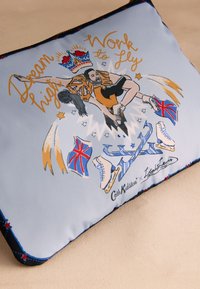 Ljusblå kudde med färgglad grafisk design och text. Illustrationerna inkluderar skridskor, en krona och flaggor. Kantad med mörkblått.