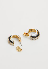 Gouden hoopoorbellen met zwart-witte emaille accentueringen, versierd met heldere strass steentjes langs de buitenrand. Voorzien van een veilige post-back sluiting.