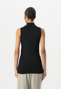 Haut sans manches noir avec un col haut, fabriqué en tissu lisse ; silhouette ajustée ; design distinct au dos, associé à un pantalon gris clair.