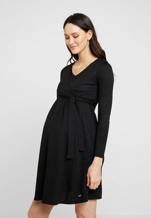 Robe de maternité noire avec des manches longues, décolleté en V, design enveloppant et une ceinture à nouer à la taille. Tissu doux, longueur genou, accents simples.