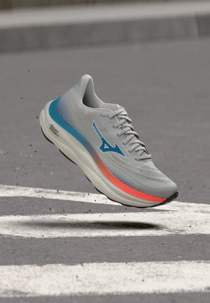 Grauer und blauer Laufschuh mit orangefarbenem Akzent scheint über einem Zebrastreifen auf Asphalt in der Luft zu schweben und zeigt Bewegung und leichte Schmutzpartikel.