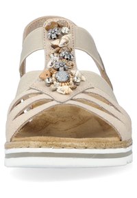 Sandali beige con cinturini traforati, impreziositi da conchiglie e perline sulla parte anteriore. Sottopiede texturizzato e suola a righe bianche.