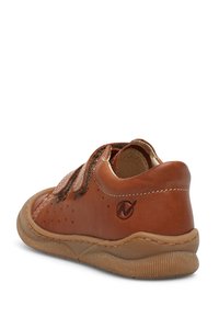 Hnědé kožené boty se dvěma suchými zipy, zaoblenou špičkou, perforovaným vzorem a flexibilní gumovou podrážkou. Na patě se nachází decentní logo.