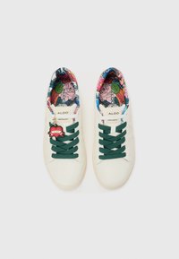 White sneakers with green laces, featuring a colorful floral-patterned insole and logo tag. Smooth material with a rounded toe design.