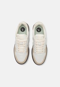 White and light tan sneakers with a smooth leather upper, round toe, perforated details, and green insole featuring a black logo.