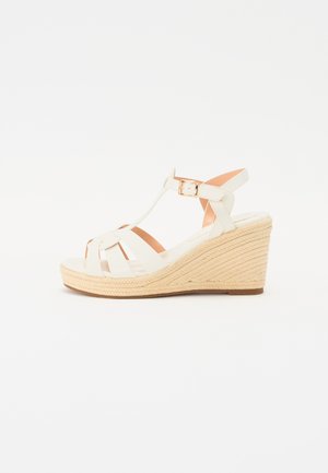 Hvide kile sandaler med et strap-design, der har en vævet jute hæl, en glat fodseng og en justerbar ankelrem med en guldbuckle.