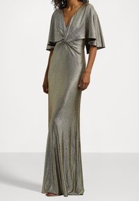 Metalická zlatá večerní šaty s hlubokým V výstřihem, splývavými rukávy ve tvaru pláště, zkrouceným předním detailem a těsně přiléhající siluetou. Hladká textura.