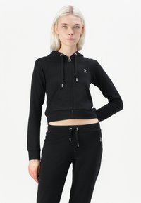 Czarna krótka bluza z zamkiem, wykonana z miękkiego materiału, z kapturem ze sznurkiem, przednią kieszenią i detalem logo. Połączona z pasującymi czarnymi dresami.