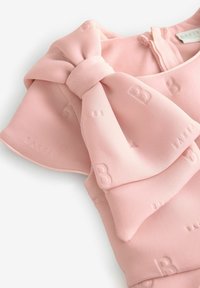 Růžový látkový top s velkým detailem mašle a embosovanými vzory "B" a "BAKER". Hladký materiál a kulatý výstřih se zapínáním na zip.