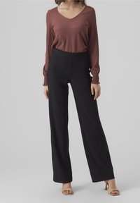 Top lungo a manica con texture bordeaux e scollatura a V, abbinato a pantaloni neri a gamba larga a vita alta. Modella che indossa sandali beige con tacco alto.