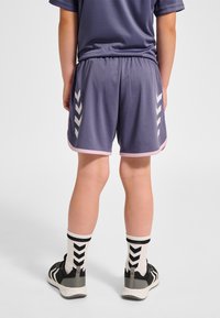 Lila sportshorts med rosa kant och sidochevronmönster, kombinerade med svarta och vita skor och strumpor med chevronmönster.