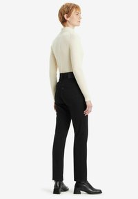 Jeans negros de tiro alto con un ajuste Slim, fabricados en denim, con bolsillos traseros y una textura suave. Combinados con una blusa de cuello alto de canalé en color crema.