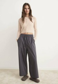 Hellrosa kurzer Pullover, graue weite Hosen mit elastischem Bund und braune Slip-On-Hausschuhe; weiche Texturen und entspannte Passform.