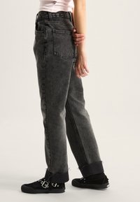 Jeans de mezclilla negros de tiro alto, con un ajuste holgado, dobladillo deshilachado, dos bolsillos traseros, combinados con zapatillas negras con hebillas.