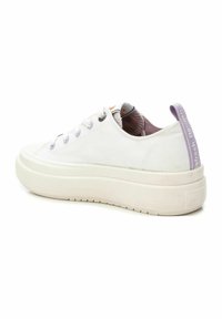 Zapatilla de lona blanca con ojetes lavanda y una lengüeta en el talón de color púrpura. Cuenta con una suela de goma blanca gruesa con patrones texturizados.