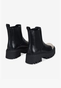 Botas Chelsea de cuero negro con paneles laterales elásticos, suela gruesa y base texturizada. Presentan una puntera en contraste para mayor detalle.