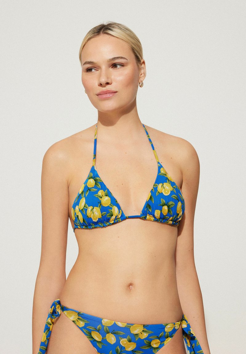 Le bikini triangle se caractérise par un tissu bleu vif avec un motif de citrons jaunes, des liens ajustables et des détails froncés en haut et en bas.